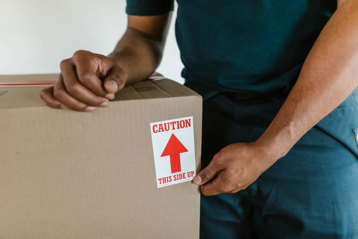 Hände kennzeichnen und verschließen einen gepackten Karton