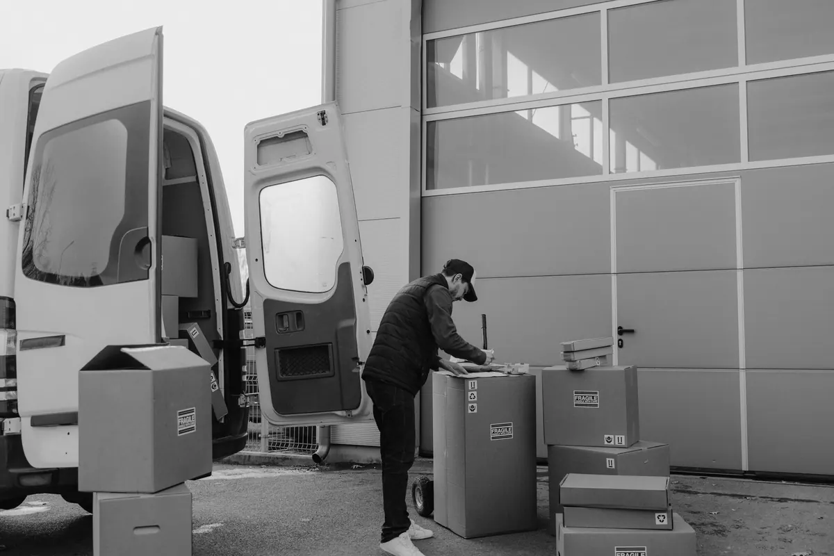 Ein Helfer lädt beschriftete Kartons in einen offenen Transporter