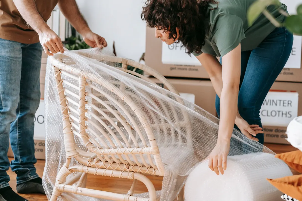 Zwei Personen schützen einen Korbsessel mit Verpackungsmaterial