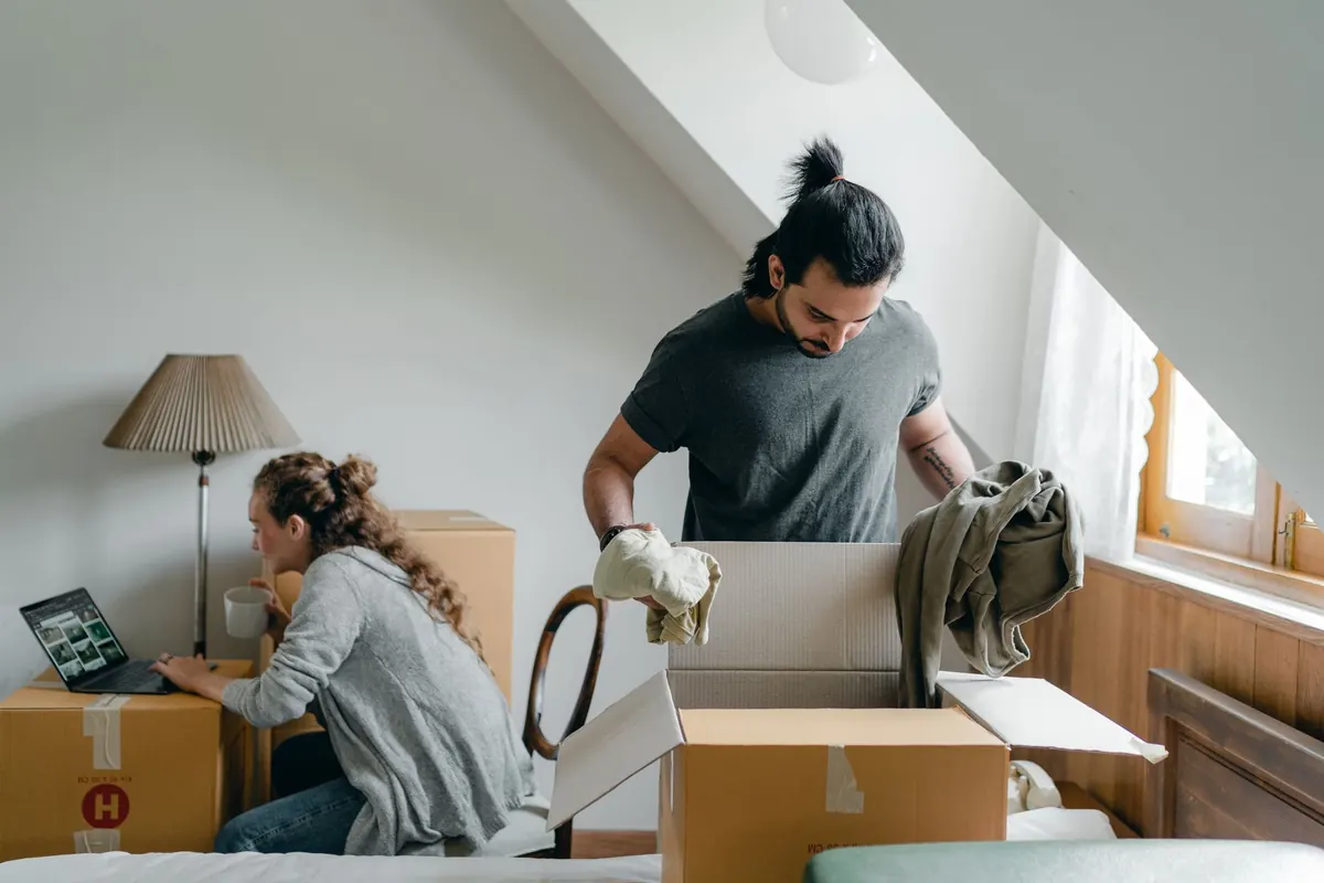 Zwei Personen packen Kartons in einer Wohnung mit Dachschräge