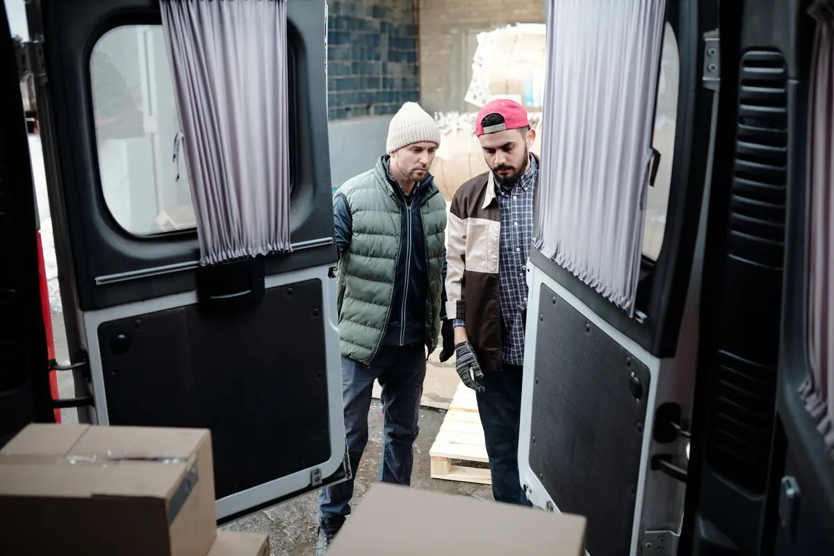 Zwei Helfer prüfen Kartons im Laderaum eines Transporters