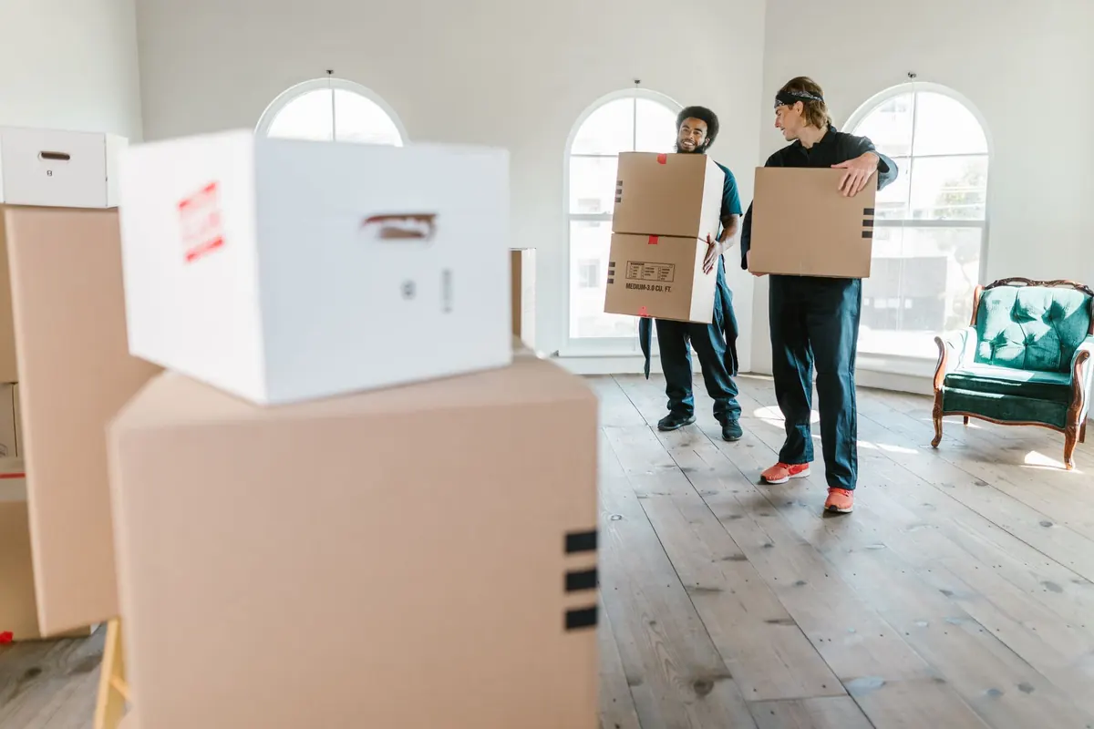 Zwei Helfer tragen Umzugskartons durch einen hellen Wohnraum